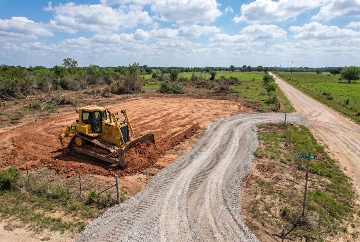 Dozer rough-grading a cleared building pad with new gravel drive to the county road, Grayson County TX